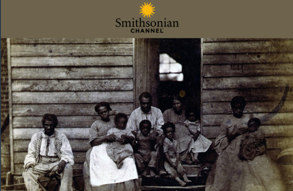 black and white photo of a slave cabin with a family of enslaved workers sitting outside