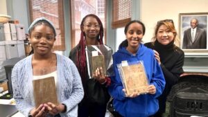 three smiling african american teenage girls stand in AARCH archives office with adult female collections manager Leone Krout