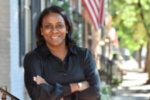 smiling woman protean gibril stands on porch in downtown frederick with black blouse and arms crossed