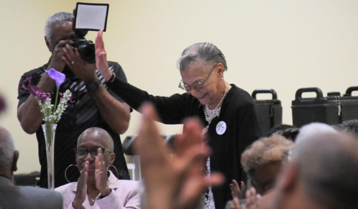 older Black woman stands up smiling and holding certificate of recognition
